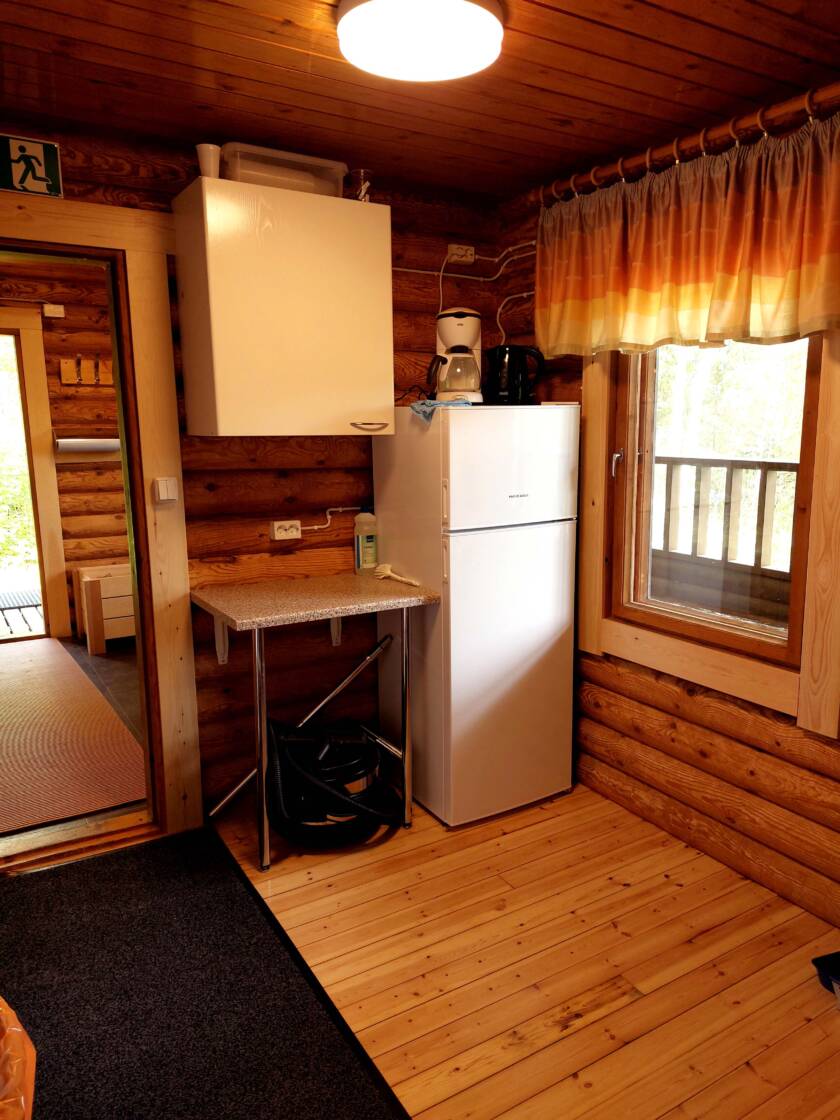 Hirsirakenteinen keittiösyvennys, ikkunan vieressä jääkaappi, taso ja seinäkaappi.