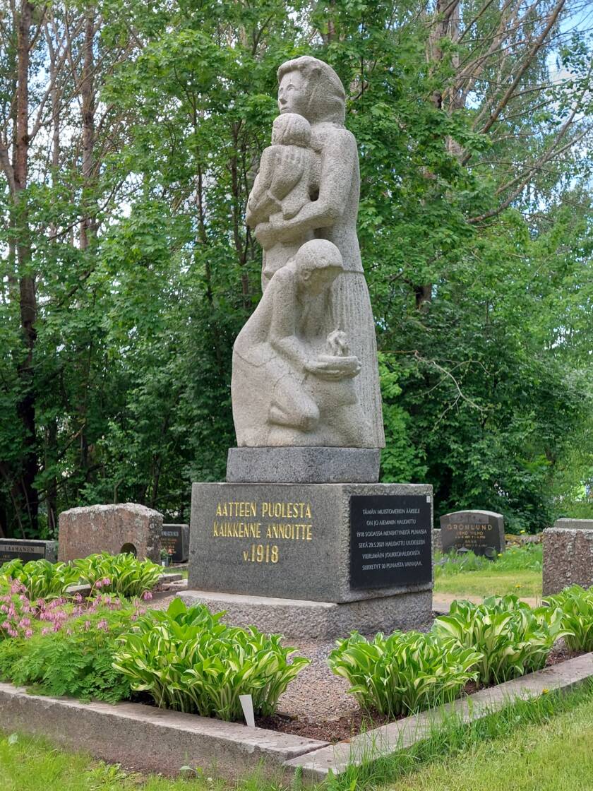 Kivestä veistetty Äiti-lapsi -patsas esittää ätiä ja kahta lasta joista toinen on sylissä ja toinen vieressä. Jalustassa teksti Aatteen puolesta kaikkenne annoitte v. 1918