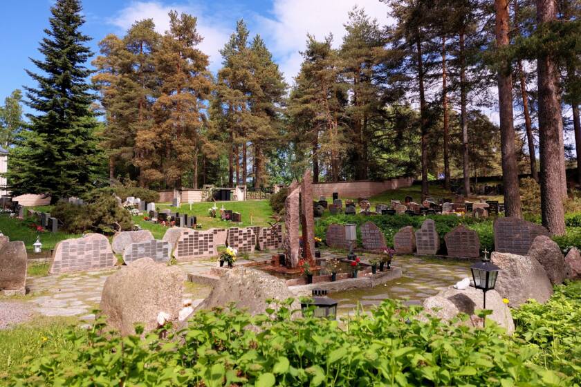 Heinolan hautausmaan muistolehto metsäisessä notkelmassa. Kivipaaseja ympyrän muodossa ja niissä metallisia laattoja.