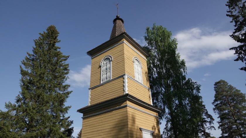 Keltainen puusta tehty kellotapuli kesäisessä maisemassa.