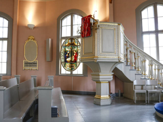 Saarnastuoli, ikkunoita, kirkonpenkkejä ja lasimaalaus sekä virsitaulu.