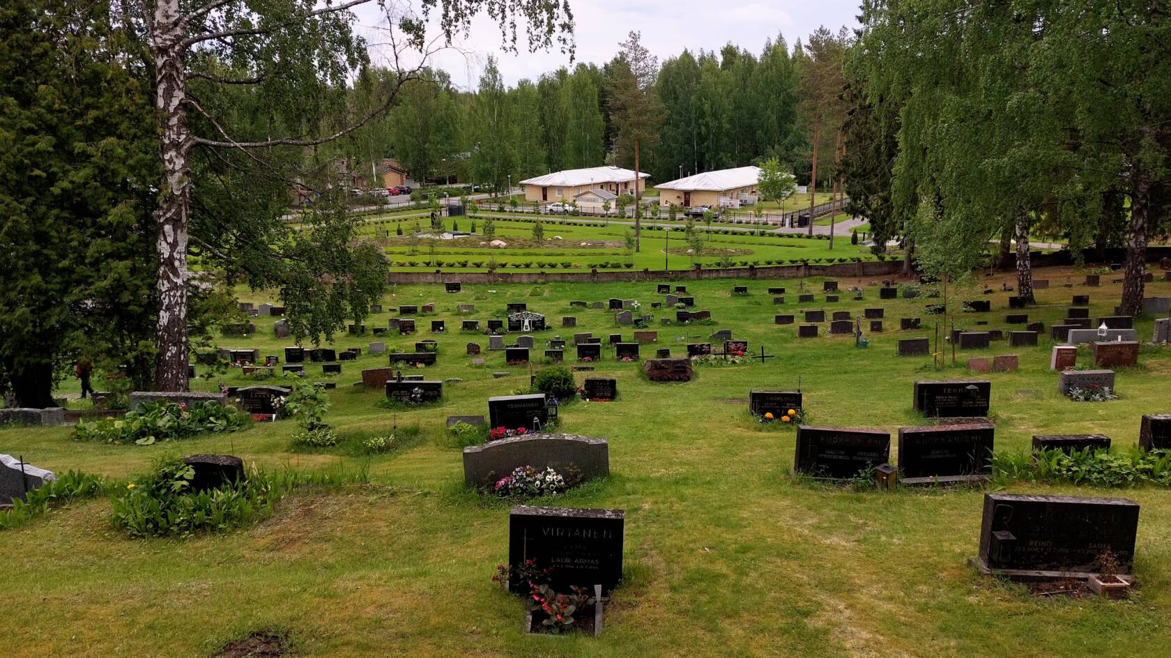Hautakiviä rinteessä hautausmaalla, välissä nurmikkoa ja puita.