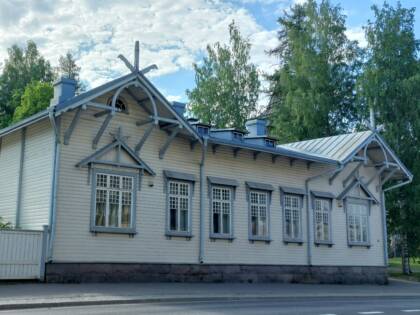 Koristeellinen 1900-luvun alun puurakennus jossa on pieniruutuiset ikkunat. Väri vaalea, ikkunanpielet harmaat.