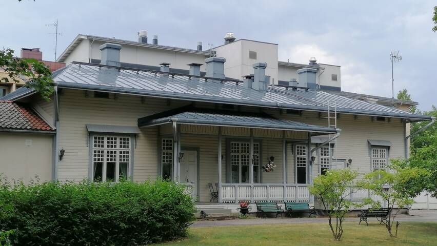 Vanha pappila on vaalea koristeellinen puurakennus 1900-luvun alusta. Ympärillä puistoa.