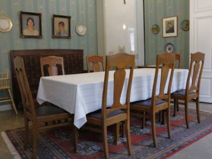 Ruokasalissa on pitkä pöytä ja koristeelliset tammituolit kahdeksalle. Seinillä koristeellinen tapetti ja muotokuvia,