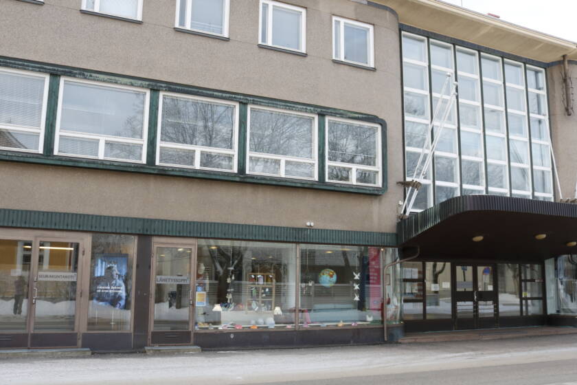 Ruskea kolmikerroksinen talo. Katutasossa isot ikkunat ja katos, jonka alla on sisäänkäynti.