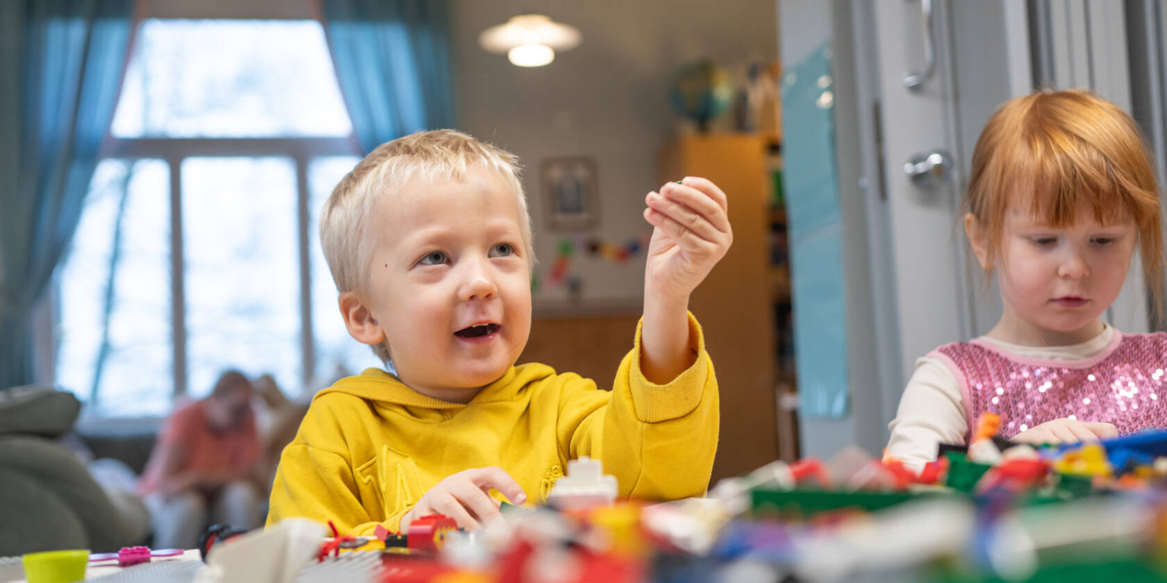 Kaksi lasta leikkii legoilla, toinen ojentaa legoa kädessään ylöspäin.