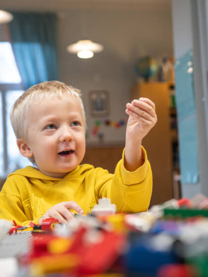 Kaksi lasta leikkii legoilla, toinen ojentaa legoa kädessään ylöspäin.