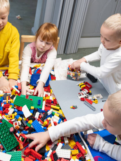 Iso kasa värikkäitä legoja pöydällä ja lapsia ympärillä leikkimässä.