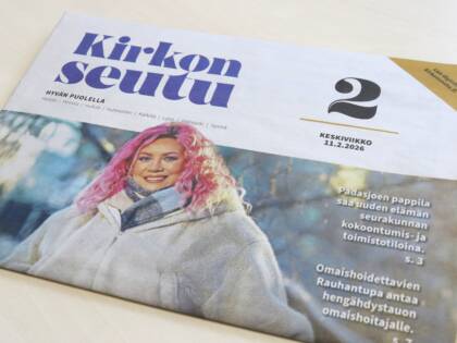 Kirkonseutu-sanomalehti pöydällä. Kannessa kuva hymyilevästä naisesta, jolla on vaalea takki ja pinkit hiukset.