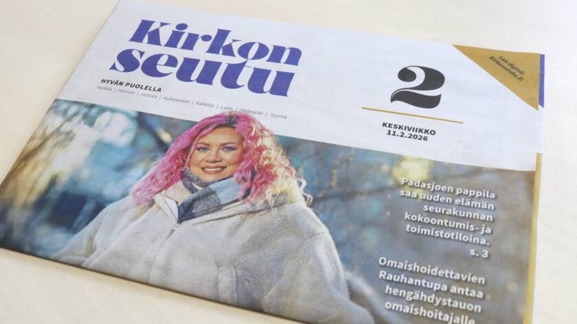 Kirkonseutu-sanomalehti pöydällä. Kannessa kuva hymyilevästä naisesta, jolla on vaalea takki ja pinkit hiukset.