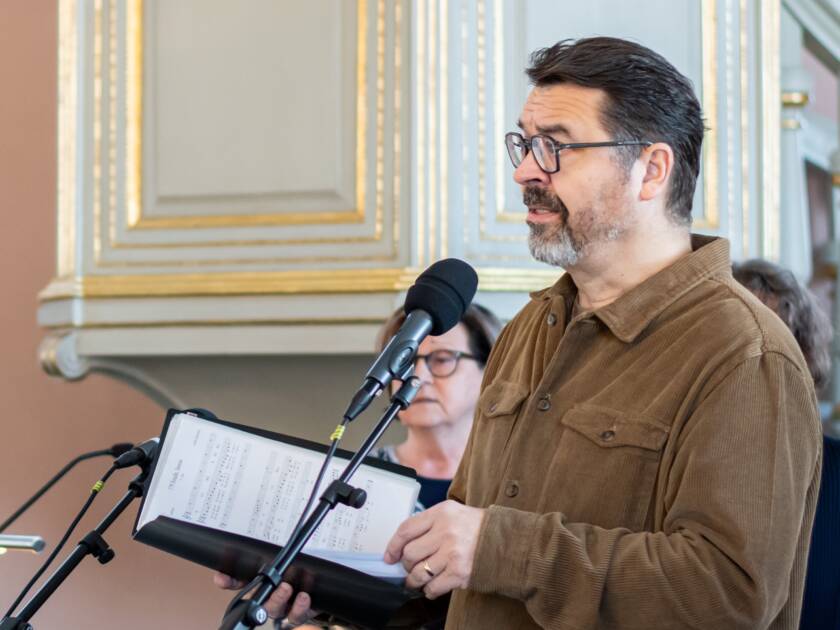Mies pitelee laulukansiota kirkossa. Taustalla nainen.