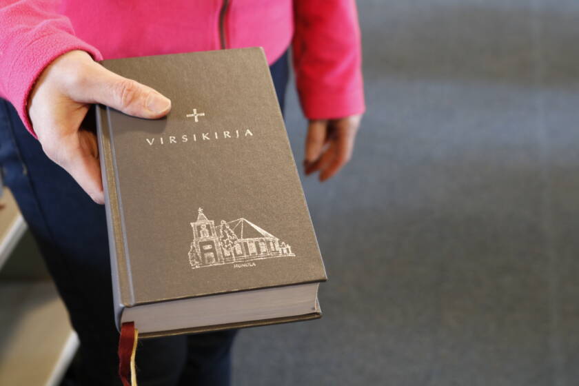 Käsi joka ojentaa virsikirjaa.