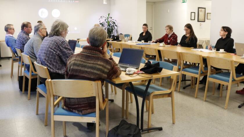 Kymmenen henkilöä istuu kokoustilassa pöytien ääressä vastakkain.