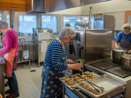 Neljä henkilöä suurtalouskeittiössä leipomassa karjalanpiirakoita.
