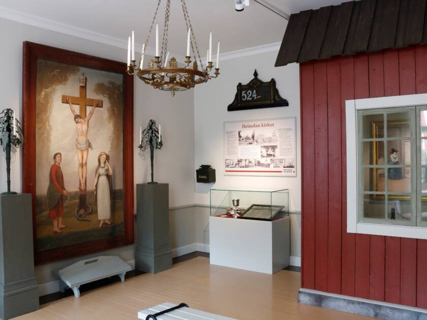 Vanha alttarimaalaus ja punaisen puurakennuksen seinää näyttelyssä museossa.