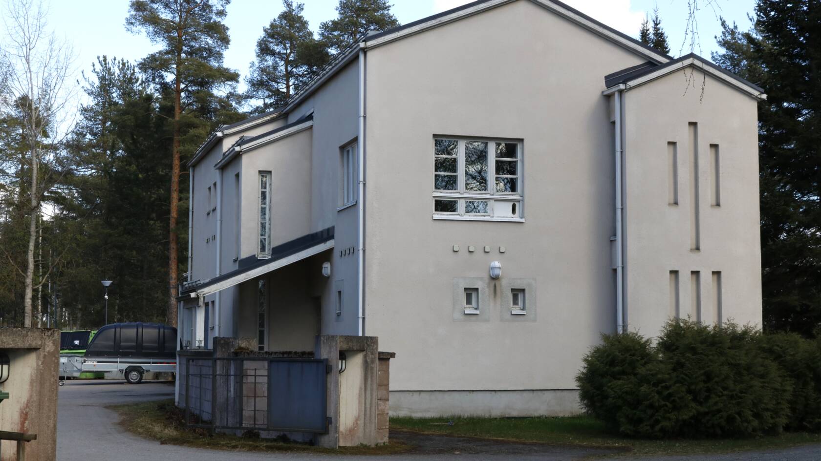 Vaalea kaksikerroksinen rapattu talo metsäisessä maisemassa.