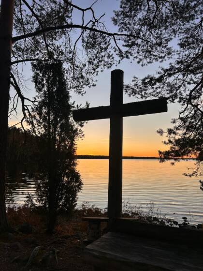 Iso puinen risti leirinuotiopaikalla järven rannalla.