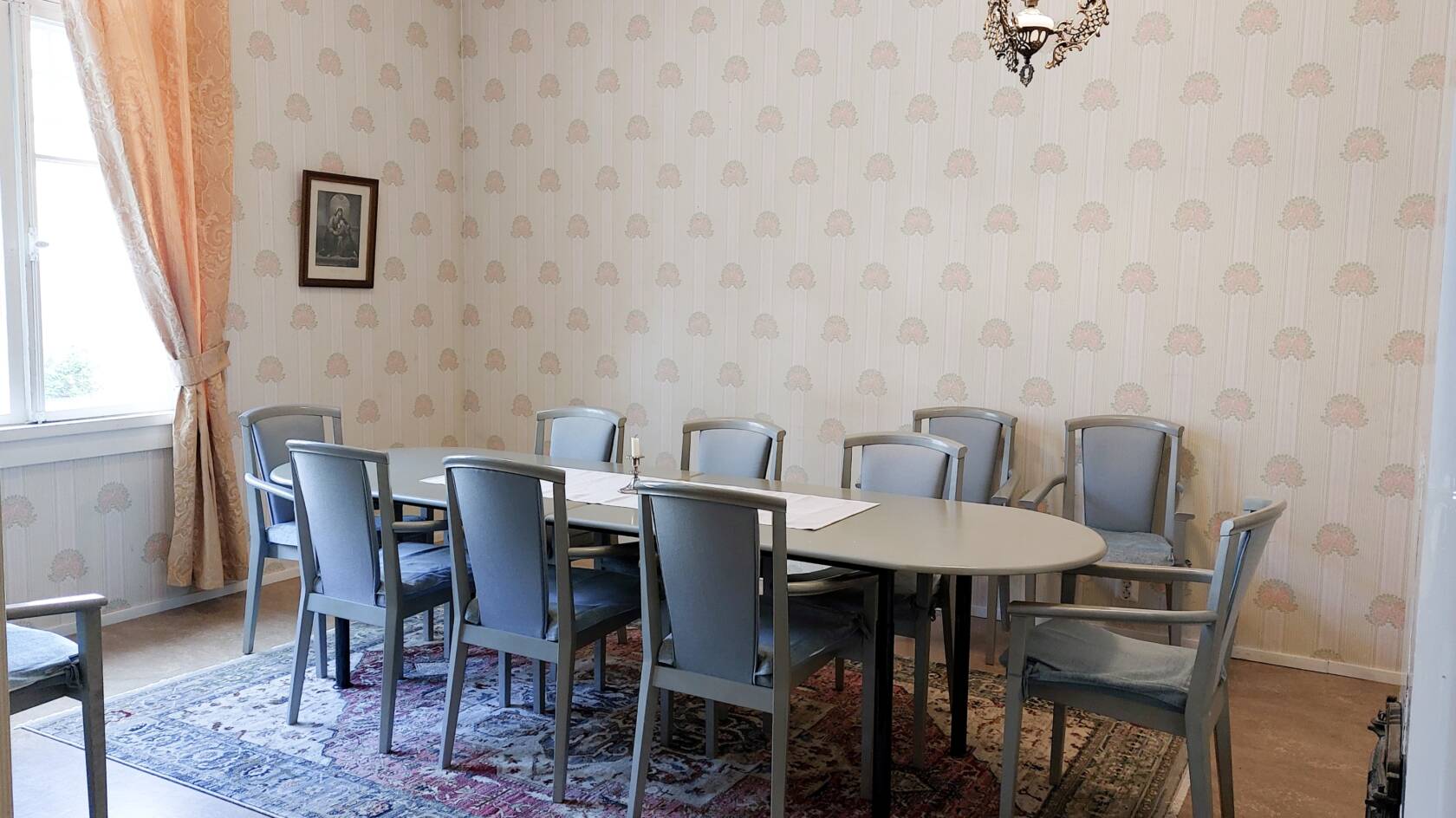 Huone, jossa on pitkä pöytä ja sen ääressä tuoleja. Seinillä vaaleat kuvioidut tapetit.