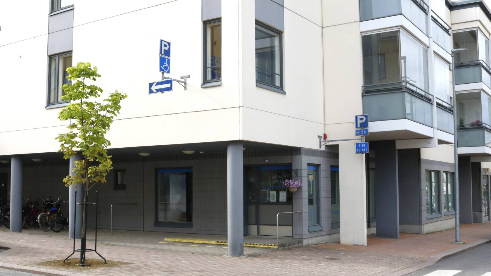 Valkoinen kerrostalo, jonka katutasossa kirkkoherranviraston lasiset liukuovet ja isot ikkunat.