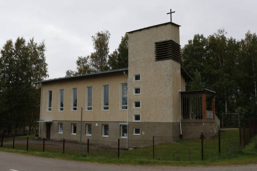 Vaalea tiilirapattu rakennus, jonka toisessa päädyssä on kellotorni. Ympärillä nurmialue.